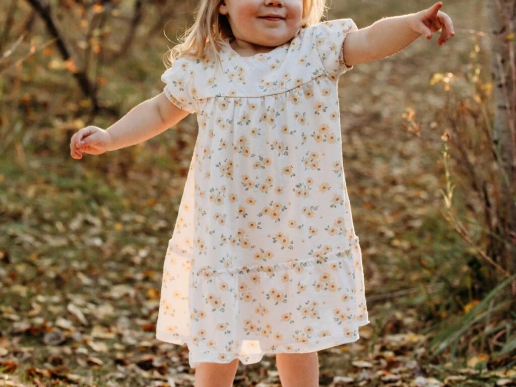 little girl wearing a sunflower dress pointing and smiling