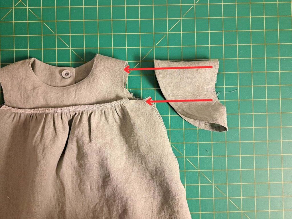 dress laying inside out and sleeve laying right side out with red arrows indicating how sleeve should go inside dress